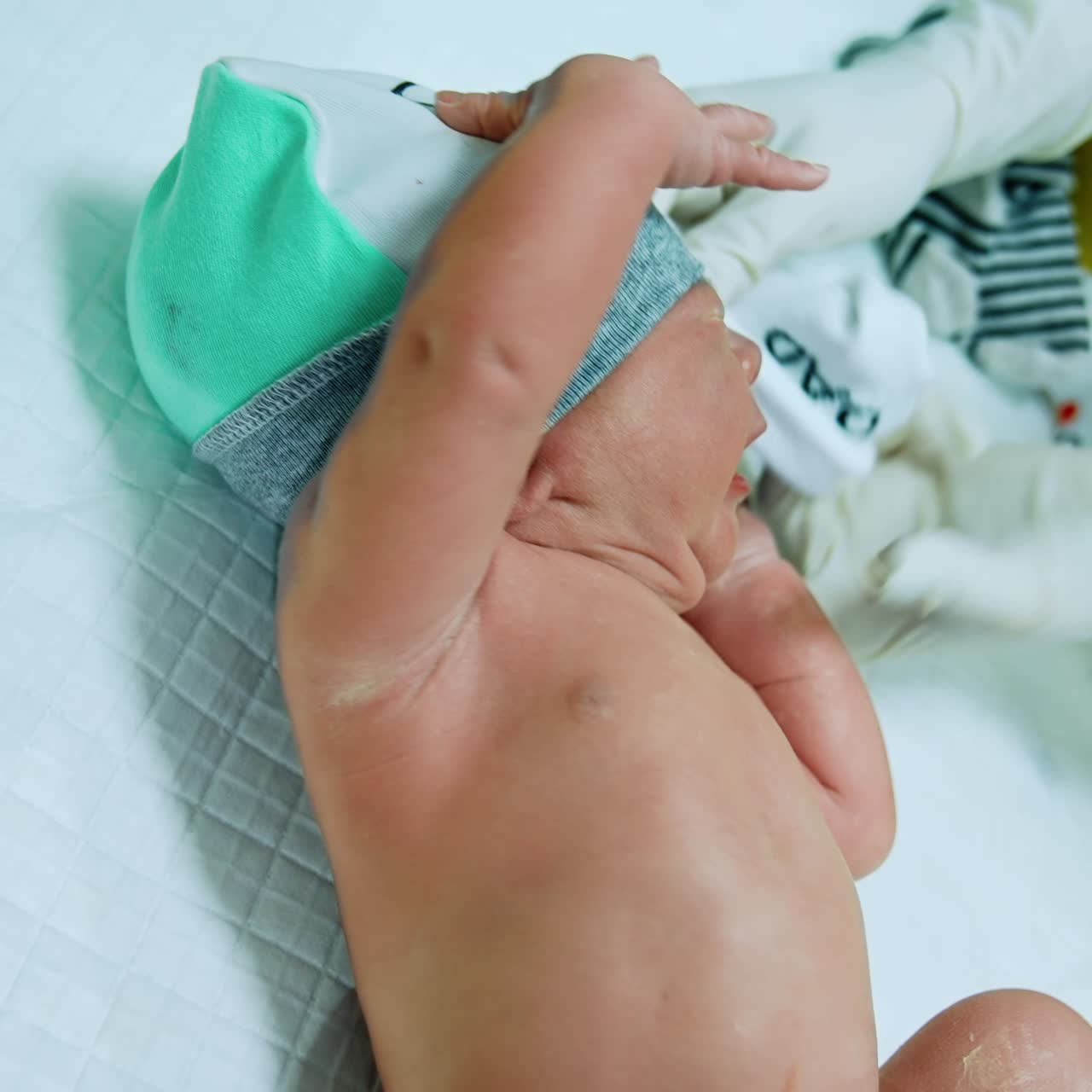 Lovely newborn baby being dressed. Child lies on the table while nurse in gloves puts mittens on tiny hands and other nurse takes care of navel