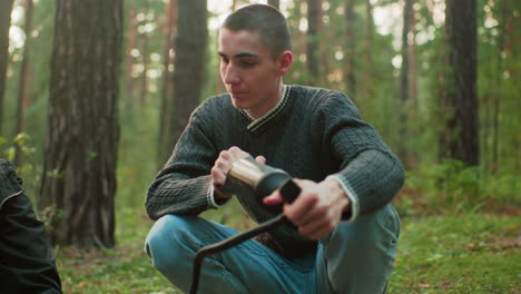 young man wearing green sweater focuses on pumping air as he glances at someone nearby, engaging in outdoor task with soft natural background and relaxed interaction