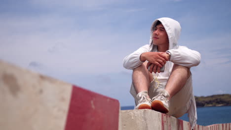 young man sits on a rock and looking at the sea - close up
