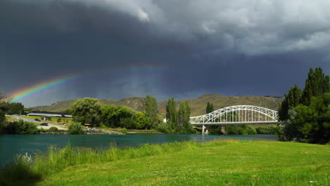 scenic static shot of a bridge, a river and a rainbow right before the rain