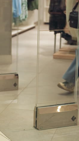 la parte inferior de las personas que salen de una tienda de ropa y zapatos se captura en este video. el video muestra la entrada de la tienda con pantallas de ropa visibles en el fondo