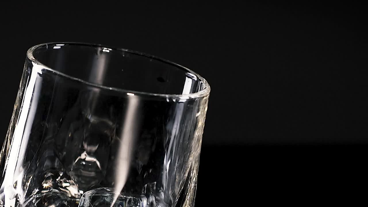A lemon slice and ice cubes rotate inside a clear glass against a black background.