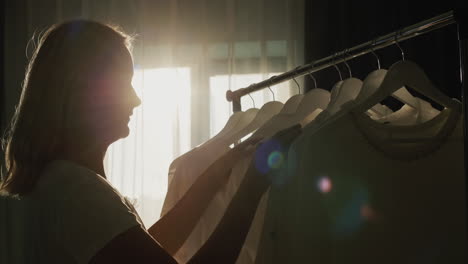 a woman chooses clothes in the dressing room. silhouette in the sun, side view