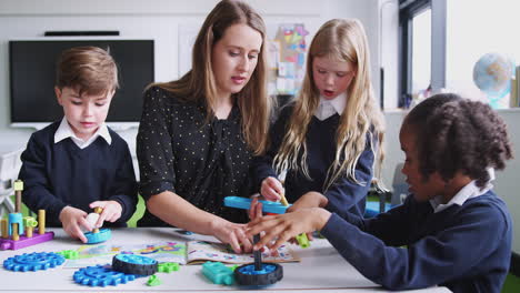 Female-teacher-helping-kids-working-with-construction-blocks-in-a-primary-school-classroom,-close-up