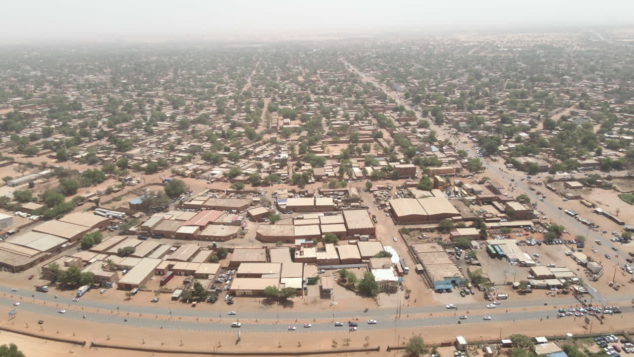 Un drone si muove all'indietro sopra una città nigeriana di giorno, rivelando un ampio paesaggio urbano e la disposizione architettonica dall'alto