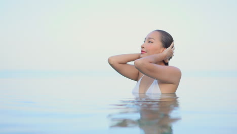 high key shot of young woman strokes her wet hair in pool