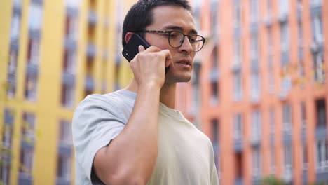 un joven japonés serio hablando por teléfono móvil mientras está de pie al aire libre en la calle 3