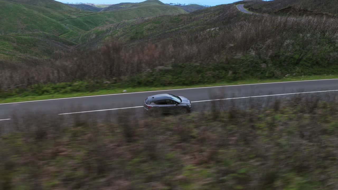 Car driving on road through mountainous landscape, Porto Moniz region, Madeira, Portugal. Aerial drone, low flight