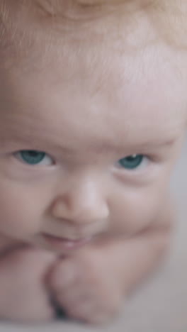 cute infant boy with large blue eyes and blond hair lies on stomach and skilled nurse practices massage close view