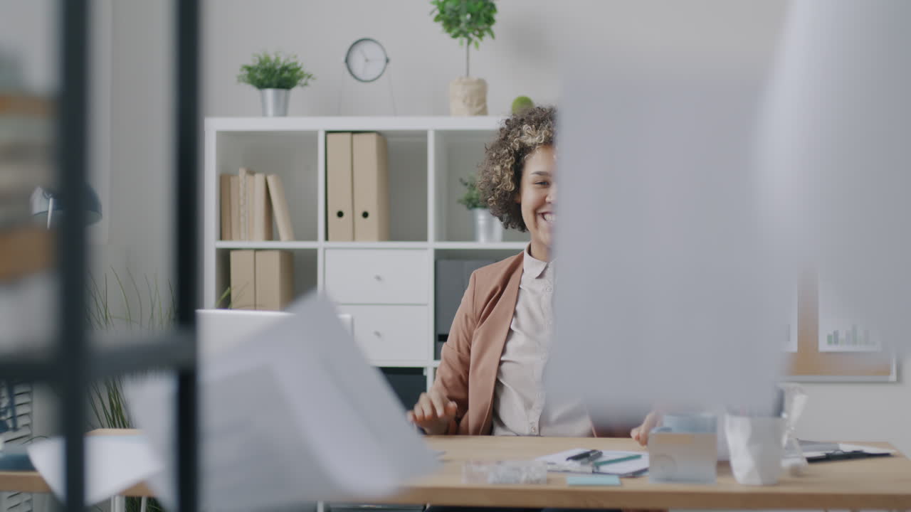 Donna alla sua scrivania in ufficio che sorride, tenendo in mano dei documenti