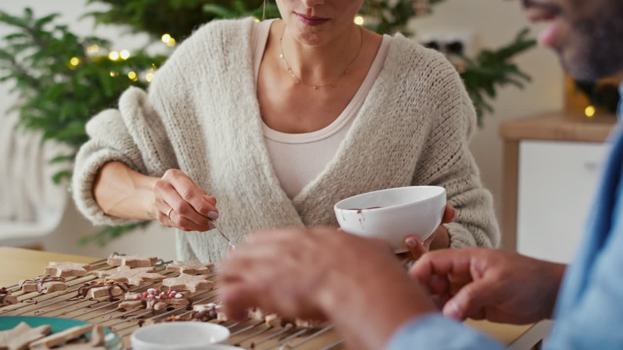 una pareja multiétnica decorando galletas dulces en casa durante la navidad.