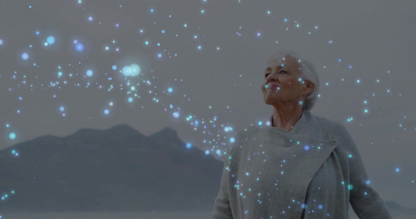 Donna anziana in piedi sulla riva che inclina e apre le braccia mentre luci blu le attraversano il viso per la salute.