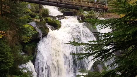 Static-close-up-view-of-beautiful-massive-Triberg-waterfall-under-wooden-bridge-during-fall-season,-Schwarzwald-black-forest,-Germany