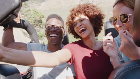 group of young friends in back of open top hire car taking selfie on summer vacation