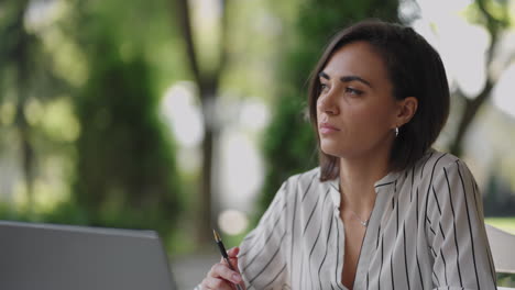 pensive woman brunette hispanic ethnic group sits at a table in a summer cafe with a laptop. serious business woman pondering problem solving and business development strategy