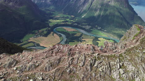 Two-Hikers-Walking-on-the-Edge-of-a-Stunning-Breathtaking-Ridge-in-Norway,-Romdalseggen,-Aerial-View-of-a-Mountain-Landscape-with-a-Beautiful-River-in-the-Background,-Drone-Flying-Sidewards