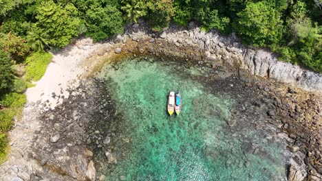 drone footage captures two boats on clear turquoise waters near a rocky, forested shoreline in phuket, thailand