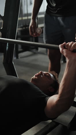 man bench pressing with trainer