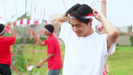 young indonesian male tying headbands against people decorating in the background