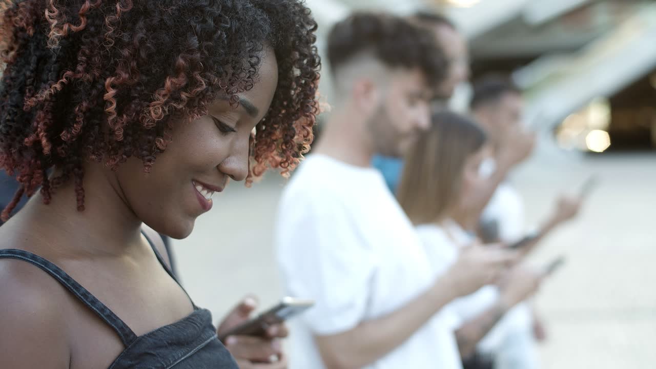 una mujer afroamericana sonriente caminando con un teléfono inteligente