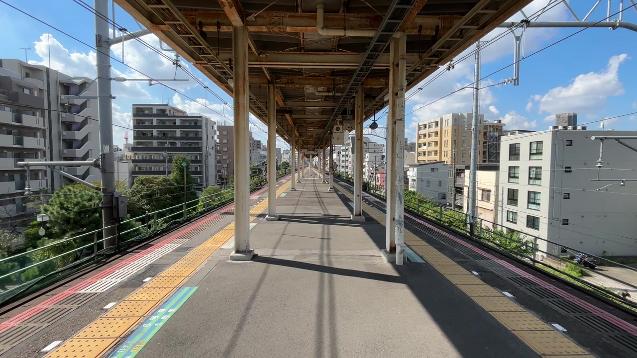 Vista di una piattaforma ferroviaria sopraelevata a Tokyo, Giappone, con edifici circostanti e cielo sereno.