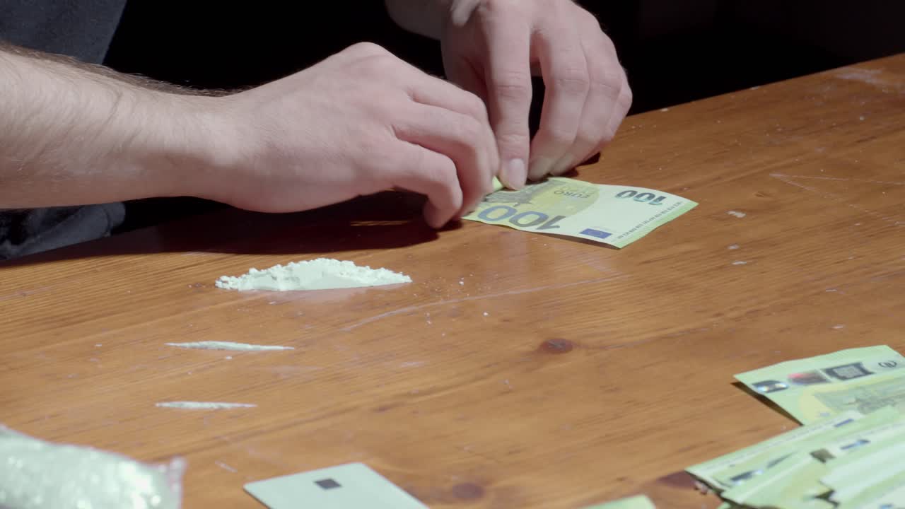 Una persona arrotola una banconota da 100 euro sul tavolo e inala cocaina in polvere.