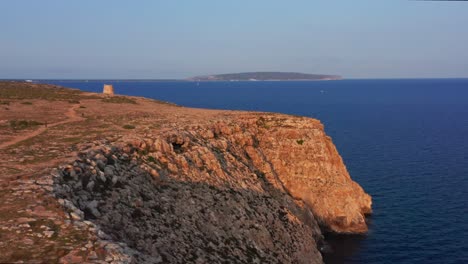 Aerial-view-of-a-dry-plain-and-rocky-cliff-over-calm-sea,-golden-hour