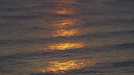 sunset casts shimmering orange glow across ocean waves