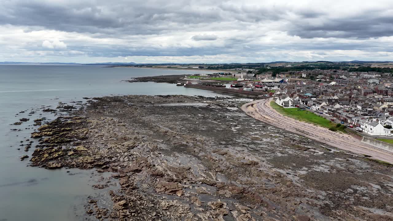 Drone camera slowly pans over rocky shoreline, coastal town, and North Sea under cloudy daylight