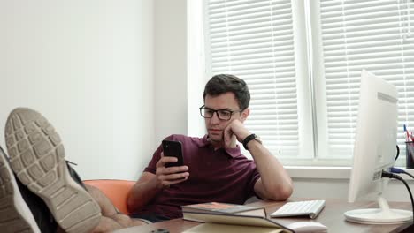 young worker in glasses relaxing with his legs on the table modern office using phone. bored manager surfing in internet. shot 4k