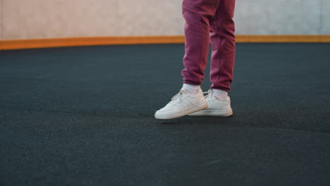 closeup leg view of female runner lifting leg up and down in white canvas sneakers on dark outdoor court under soft sunset light showing motion and fitness energy dynamic posture and intent focus
