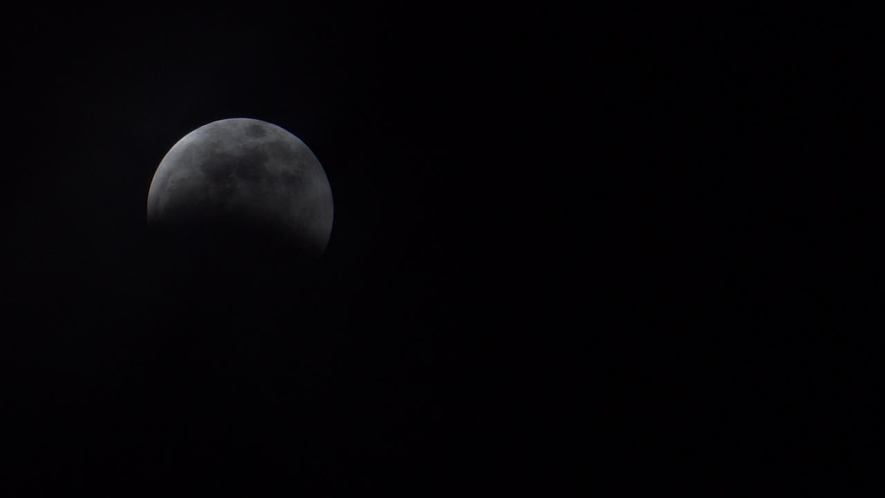 Thin clouds slowly reveal a full moon during a lunar eclipse