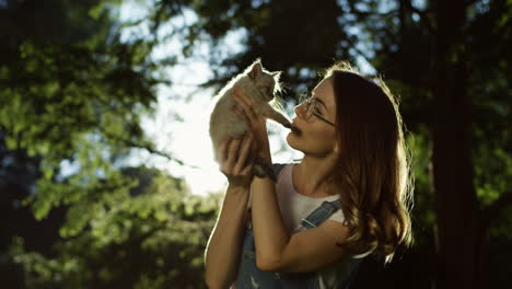 young caucasian woman in glasses holding little kitty cat and petting it in the park on a summer day