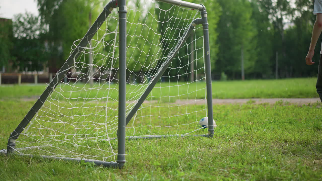 маленький мальчик с энтузиазмом пинает мяч к ворота в то время как его старший брат движется, чтобы перехватить, на заднем плане, люди размыты