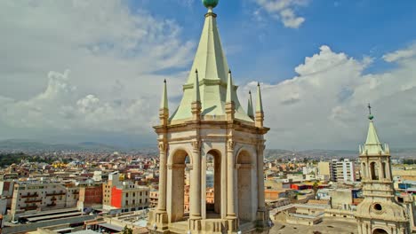 La-Toma-De-Un-Dron-Desciende-Desde-La-Torre-Izquierda-De-La-Catedral-De-Arequipa,-Con-Nubes-Distantes-Y-La-Pequeña-Torre-Izquierda-A-La-Vista.