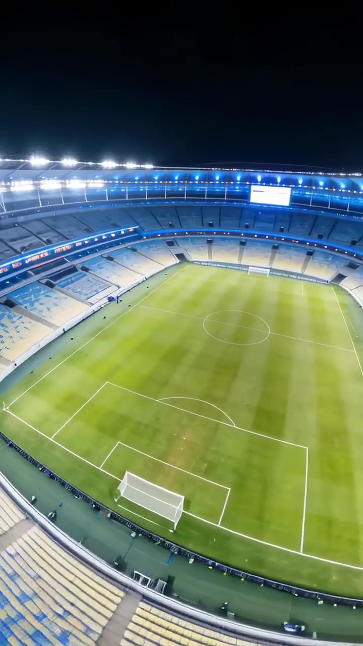 Video verticale: Una telecamera rotante rivela uno stadio vuoto di notte, con il personale in abiti ad alta visibilità che si prepara per la partita.
