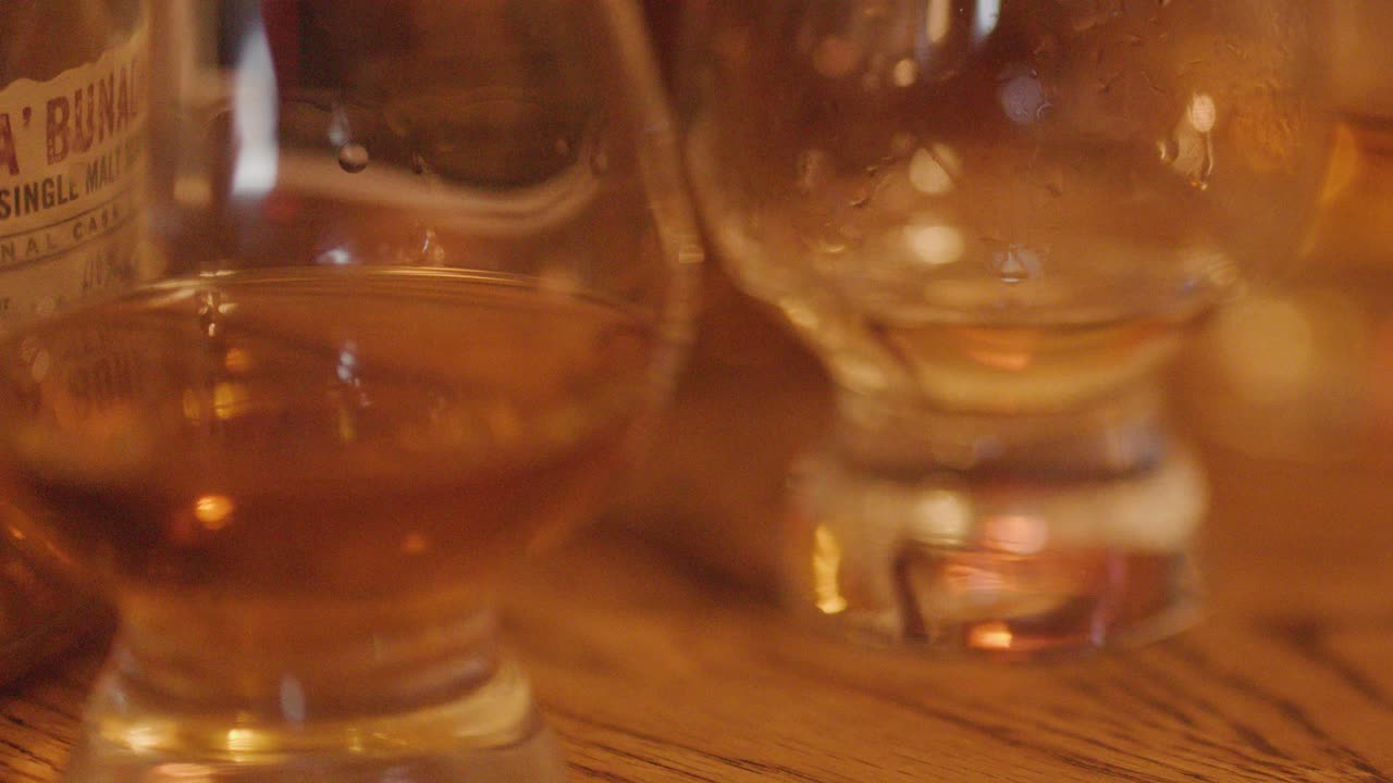 Slow pan of whiskey glasses and bottles on wooden table in warm, cozy indoor lighting