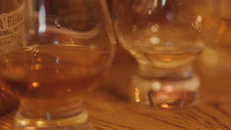 slow pan of whiskey glasses and bottles on wooden table in warm, cozy indoor lighting