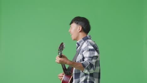 녹색 화면 배경에 록 음악과 함께 기타를 연주하는 젊은 아시아 십대 소년의 측면 시각