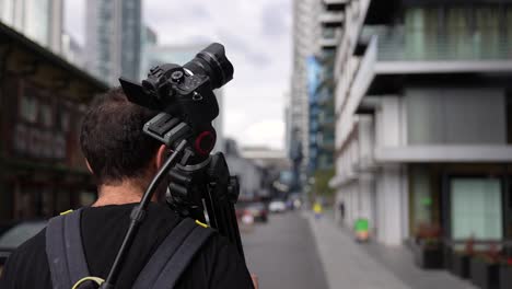 Close-up-of-a-young-caucasian-man-is-walking-with-his-backpack-and-camera-tripod-on-his-back-in-the-streets-of-the-business-district-Canary-Wharf-in-London-in-autumn