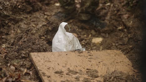 close up of hooded captive man lying on dirt ground with hands tied as military personnel place wooden board over him