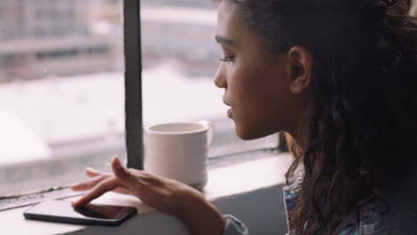 beautiful-hispanic-woman-using-smartphone-at-home-drinking-coffee-browsing-messages-enjoying-texting-on-mobile-phone-messaging-social-media-sharing-student-lifestyle-in-apartment-loft