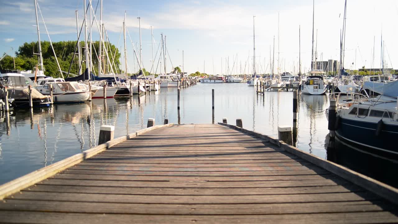 Small wooden pier leading towards the waters of a sail boat harbour during sunset in the Netherlands