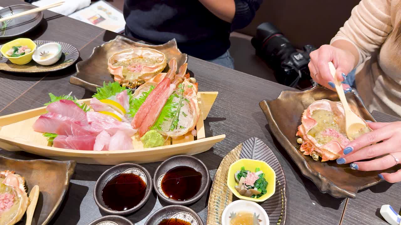 日本の東京にあるレストランで、新鮮な刺身の舟盛りとカニ味噌を楽しむ食事客。