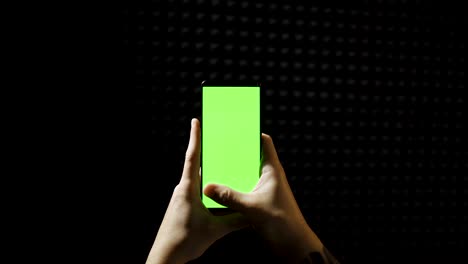 hand scrolling smartphone with green screen isolated on black background