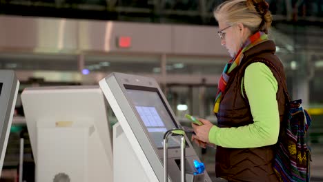primer plano bajo de una mujer con pasaporte y teléfono inteligente en la mano, en una terminal de autocomprobación del aeropuerto y registrándose a sí misma