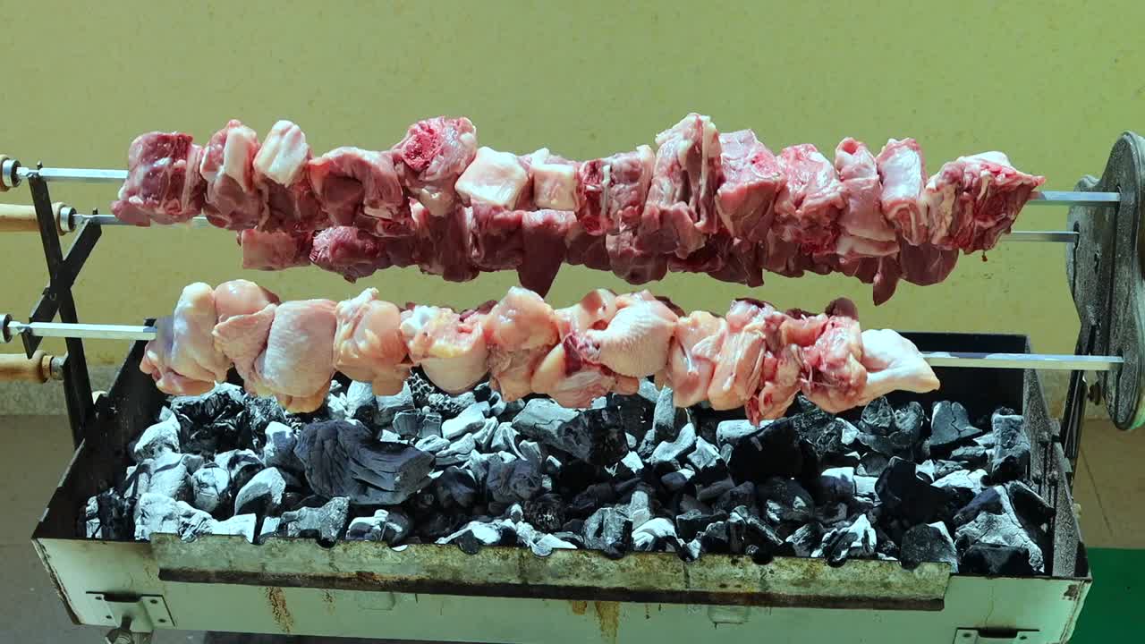 Nahaufnahme von Hähnchen und Schweinefleisch, das auf einem heißen Grillrost über Holzkohlefeuer gart. Das Fleisch brutzelt beim Garen mit sichtbarem Rauch und Hitze. Ideal für Lebensmittelwerbung, Outdoor-Kochinhalte, Sommergrillen.