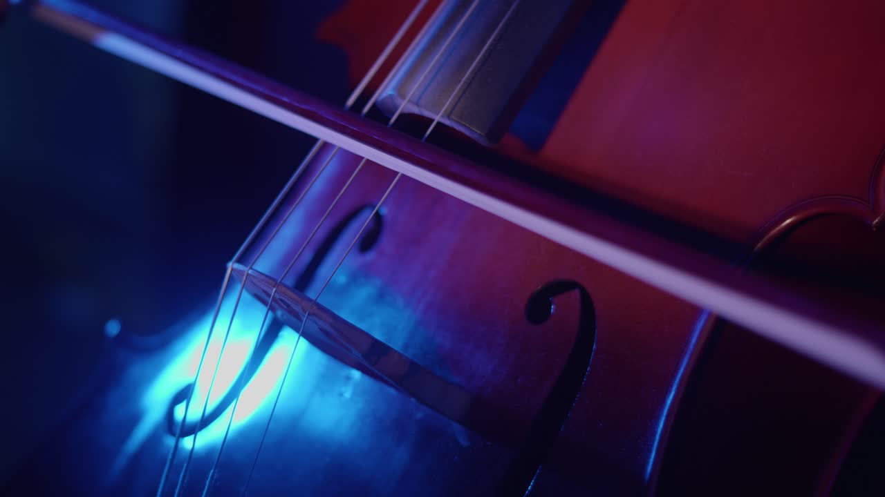 Close-up of Cello Strings Being Played with Bow Under Dramatic Lighting