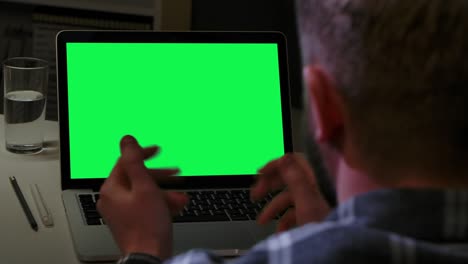 vista desde atrás hombre hablando en comunicación de video y mirando pantalla verde chroma clave portátil mientras está sentado en la oficina de casa. trabajo remoto, educación en línea en casa. cerca. cámara lenta