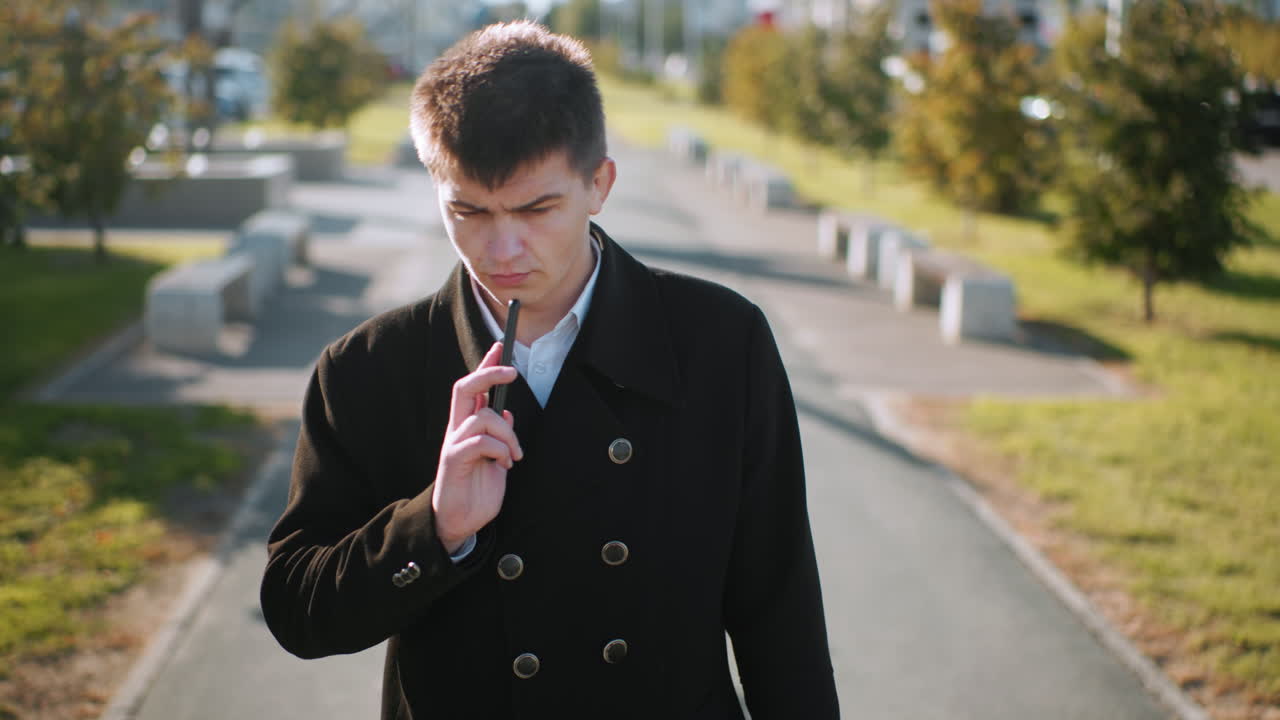 검은 코트를 입은 은행가,  에 전화를 들고, 통화를 할 때 하고, 사려 깊은 모습을 보이고, 현대적인 유리 건물, 부드러운 빛, 나무, 포장된 경로와 함께 도시 환경